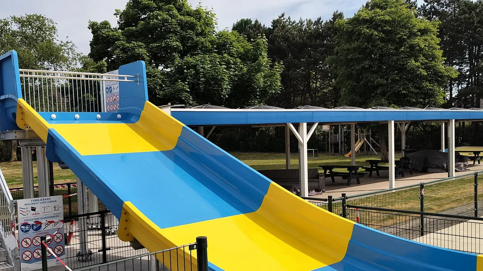 Brede geel-blauwe glijbaan met stalen trap aan een buitenbad