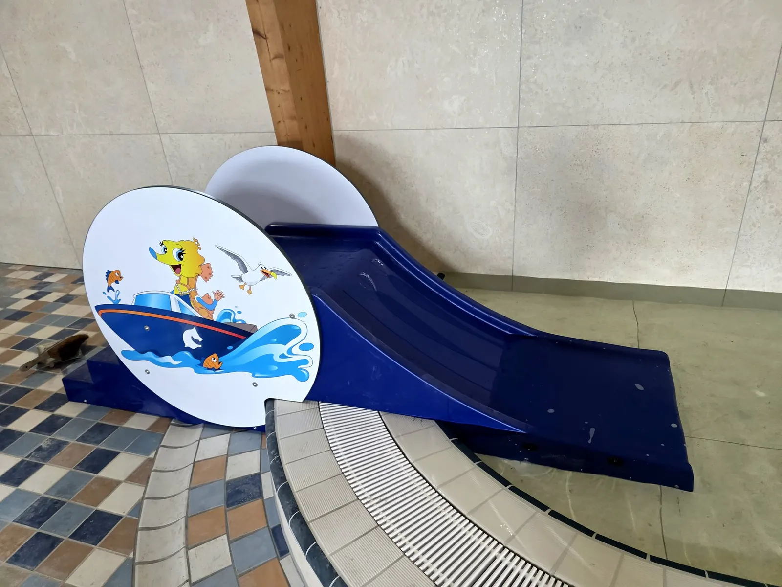Kleine blauwe peuterglijbaan met een vrolijk paneel in de waterspeeltuin van Paardekreek